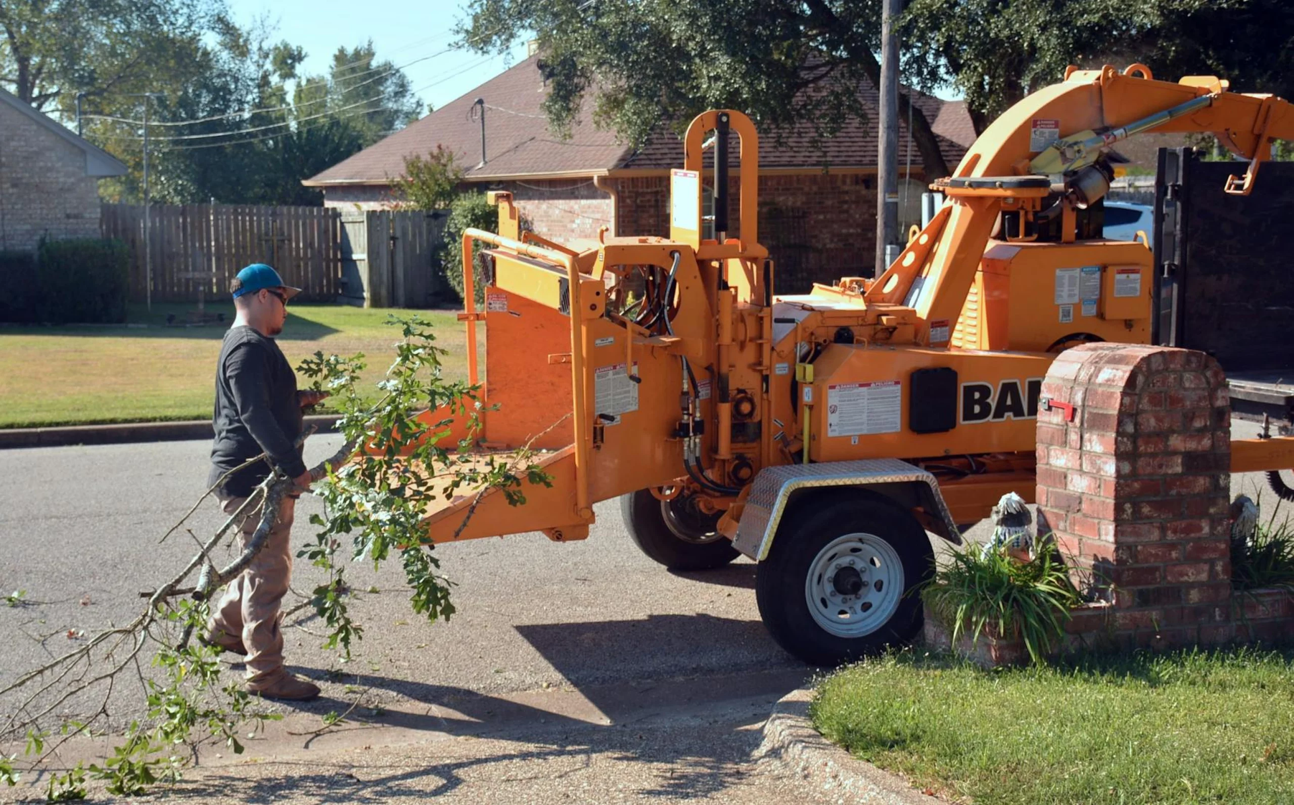 Professional landscaper feeding tree branches into wood chipper during residential tree removal in Morris County